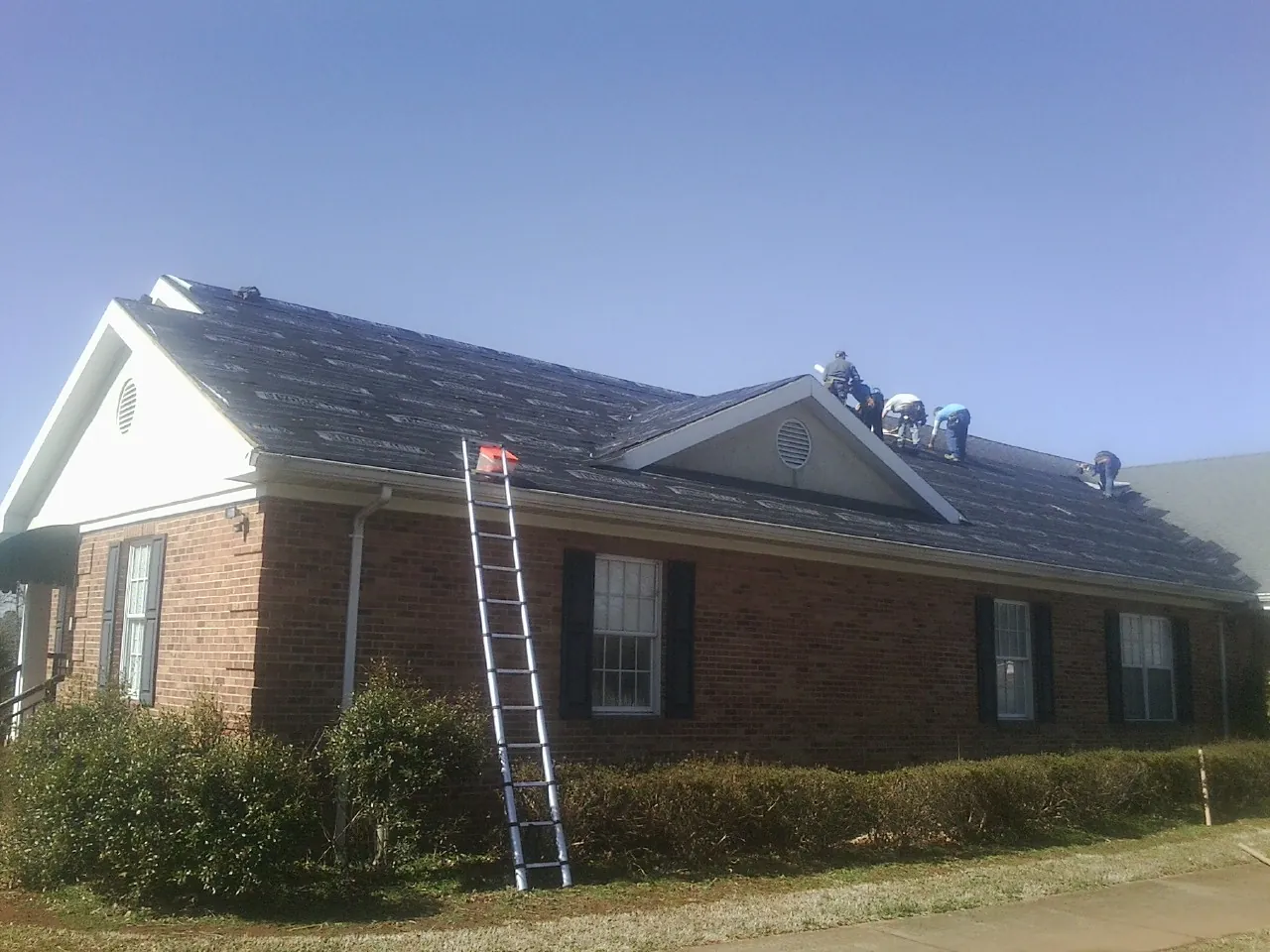 Crew tearing shingles off a brick ranch roof with a ladder set — Emergency Roof Repair work by our crew in Pine City