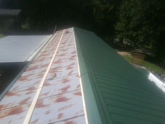 Old rusted panels beside newly installed green metal roofing — Wind Damage Roof Repair by Roofing Brothers in Pine City